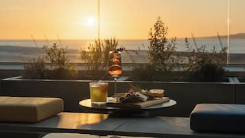 A table with a glass of iced beverage, a bottle of wine, and a cheese board with grapes and nuts.