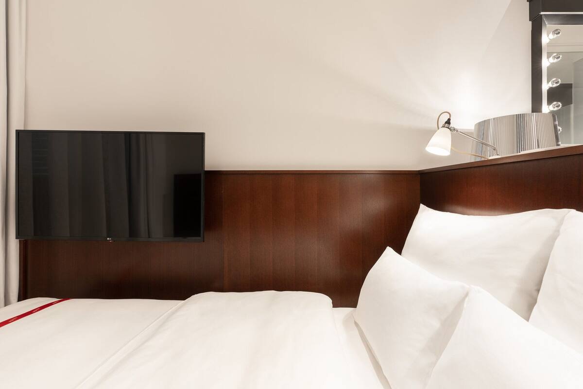 Ein Hotelzimmer mit flachbildfernseher an der Wand, einer Nachttischlampe und einem Holzkopfteil.