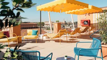 Une terrasse sur le toit, agrémentée de parasols jaunes, de chaises longues et d’une petite table sur laquelle est posée une plante.
