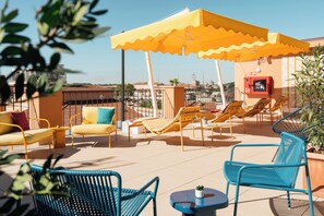 A rooftop terrace with yellow umbrellas, lounge chairs, and a small table with a plant. - Ruby Lilou Hotel Marseille by IHG (Marseille)