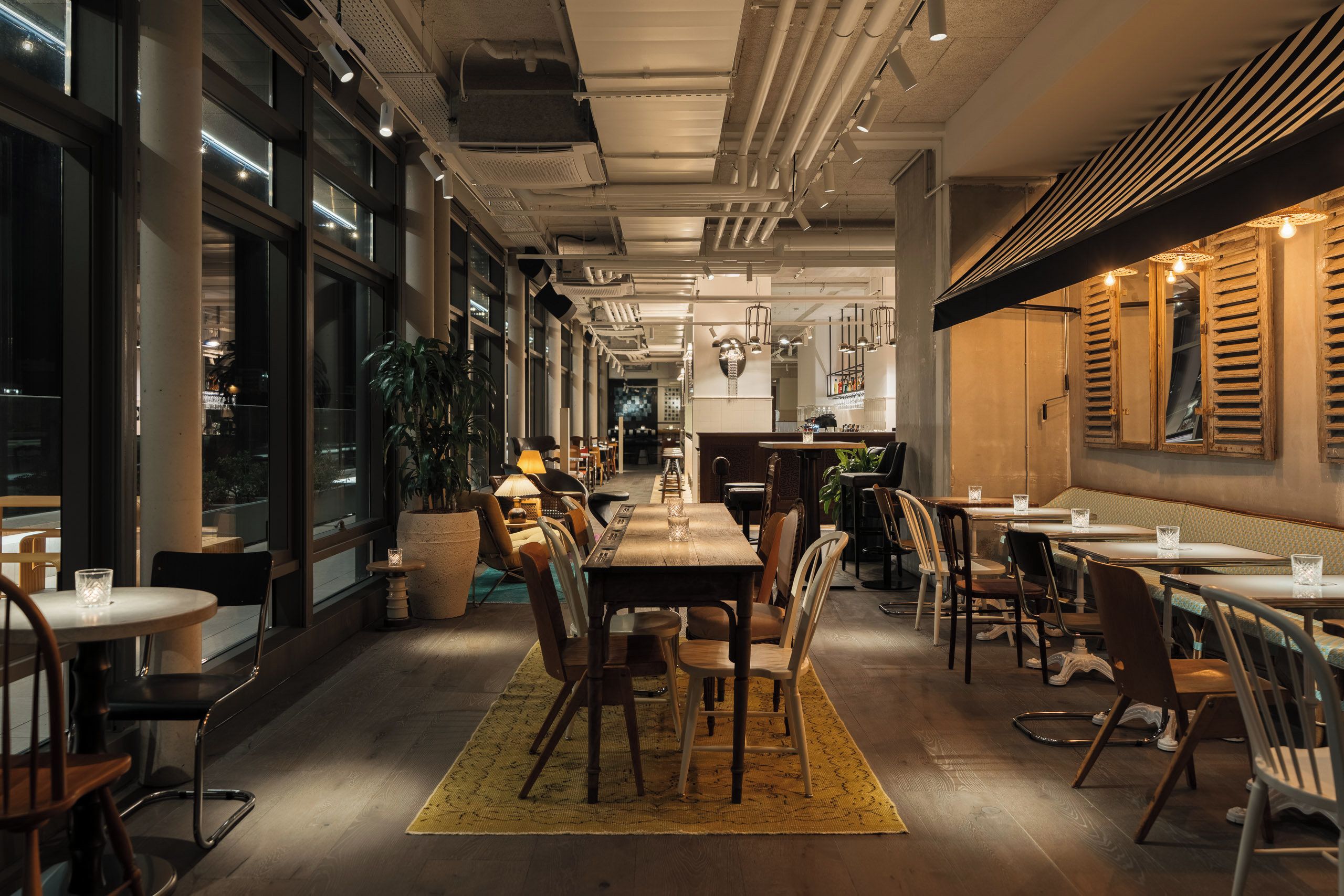 A restaurant with a long communal table, individual tables, and chairs.