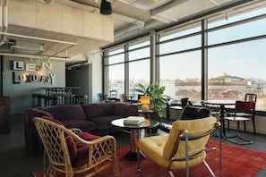 Ein geräumiges Büro mit einem großen Fenster und Blick auf die Stadt, eine gemütliche Sitzecke mit einer Couch und Sesseln, sowie eine Wand mit dem Schriftzug 'LEAN LUXURY'.
