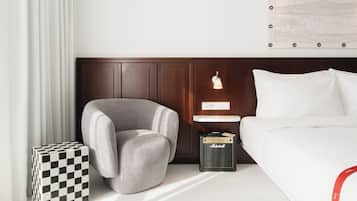 Une chambre d’hôtel avec un lit, un fauteuil gris, une petite table avec une lampe, un amplificateur Marshall et un cube à motifs à carreaux.
