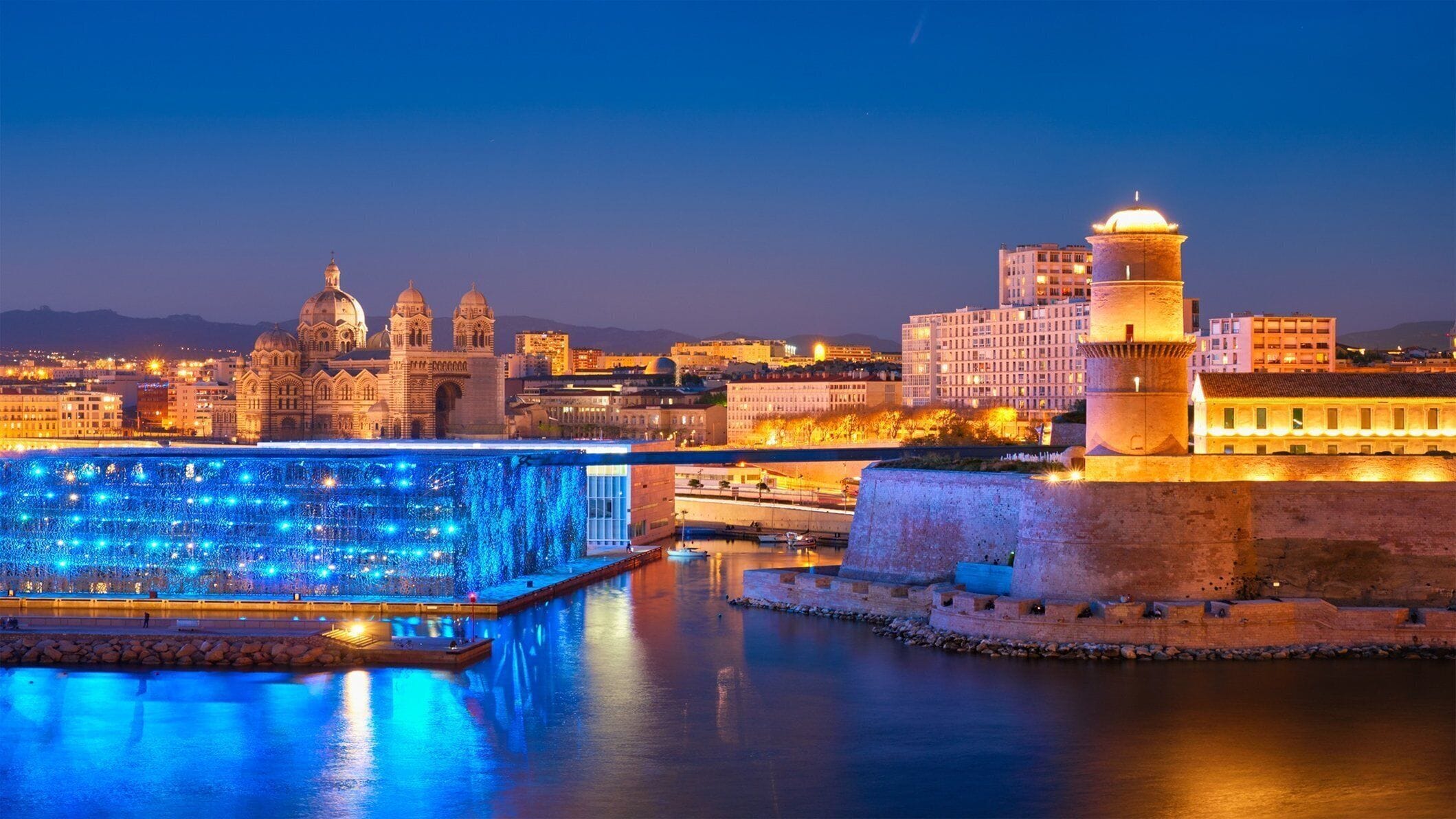 A historic cityscape with illuminated buildings and a prominent fortress.