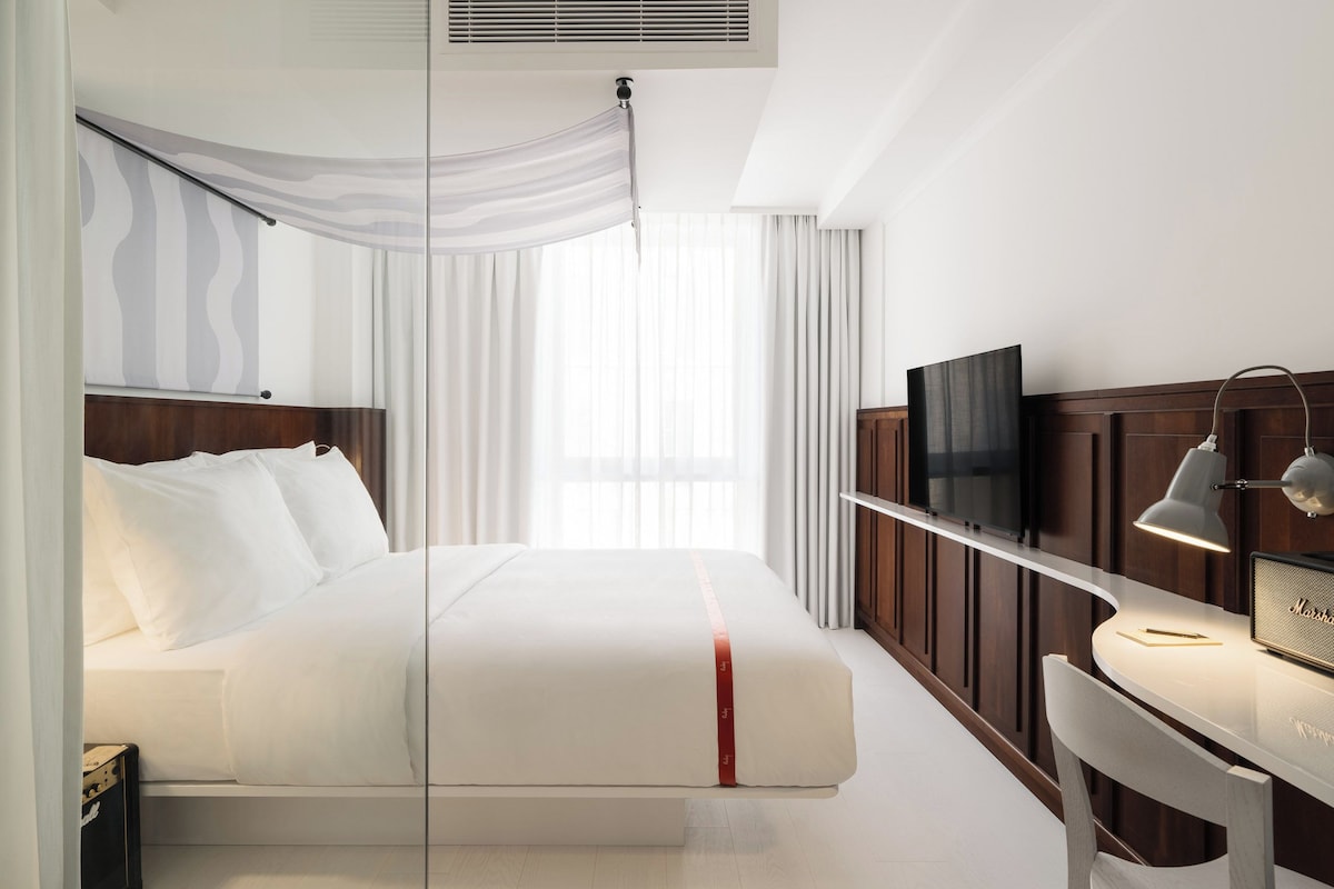 Ein modernes Hotelzimmer mit einem großen Bett, einem Schreibtisch mit Computer und einem Fernseher.