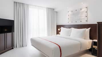 A hotel room with a large bed, a flat-screen TV, a wall-mounted artwork, and a red-striped bed runner.