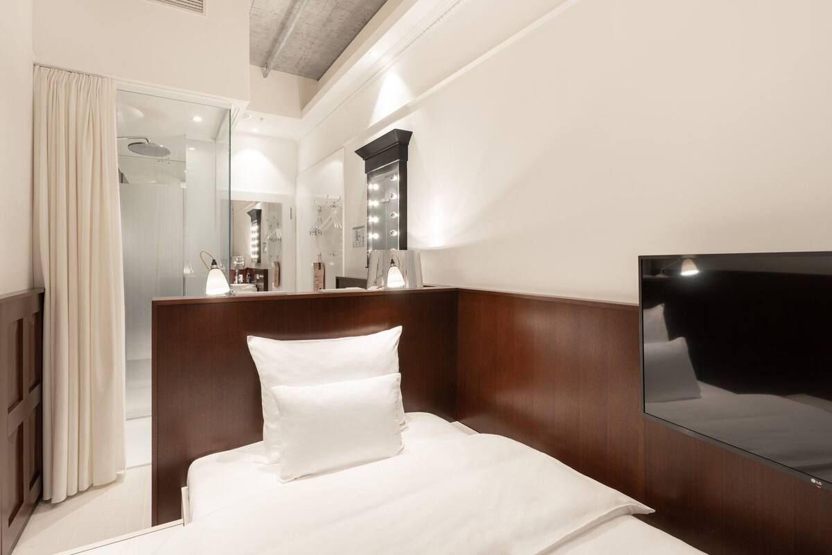 Ein Hotelzimmer mit einem Bett, einem großen Spiegel, einem Flachbildfernseher und einem durch eine Glastür einsehbarer Badezimmer.
