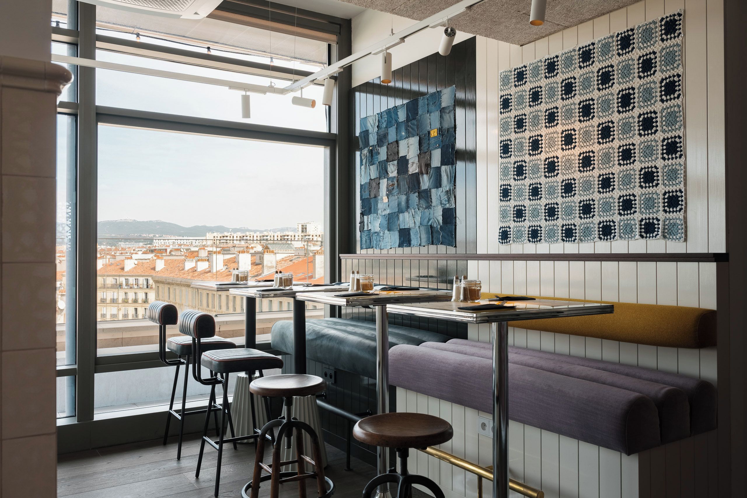 Zona de bar moderna con vistas a la ciudad, que incluye una mesa alta, taburetes y un banco.