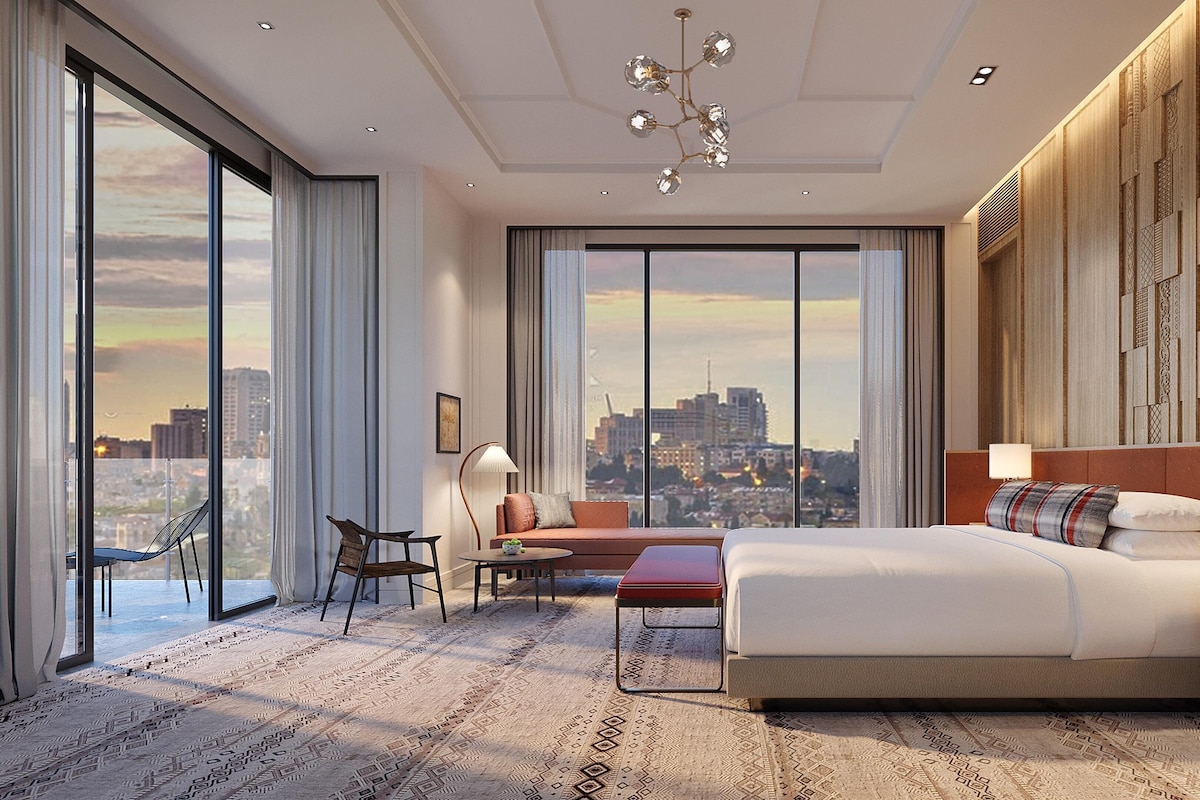 Ein modernes Hotelzimmer mit einem großen Bett, einem Schreibtisch, einem Sessel und Blick auf die Stadt.