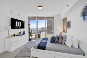 Ein modernes Hotelzimmer mit Bett, Fernseher, Schreibtisch und einem Balkon mit Blick auf die Stadt.
