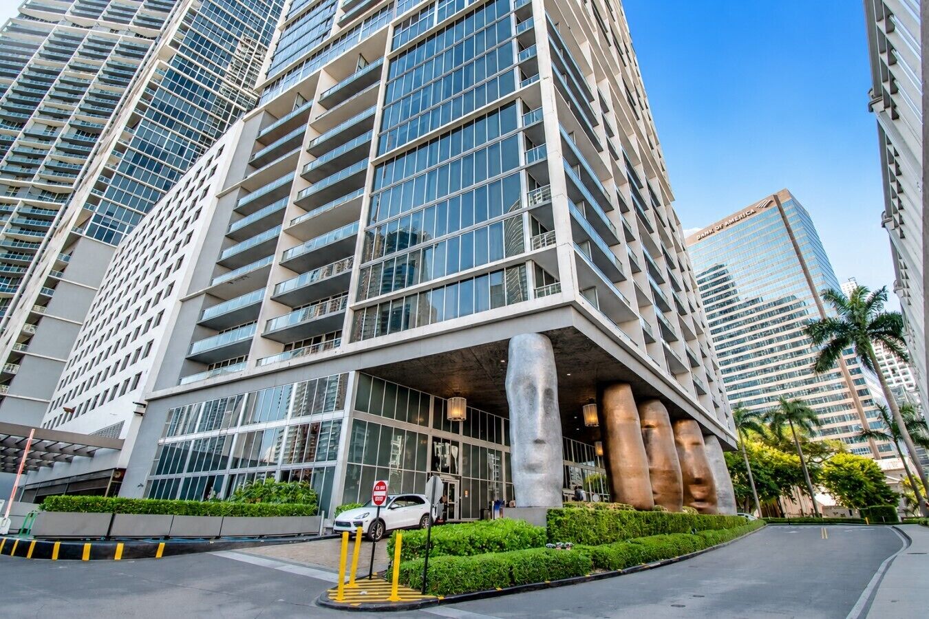 A modern high-rise building with a glass facade, multiple balconies, and a prominent entrance with a covered area.