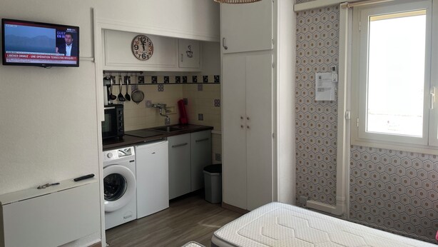 Un espacio habitable compacto con kitchenette, lavadora, comedor y ventana con papel tapiz estampado.