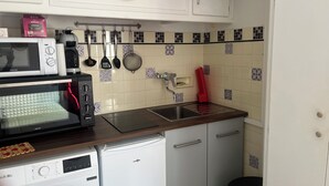 Una cocina con microondas, cafetera, utensilios colgantes, un lavabo y una lavadora.
