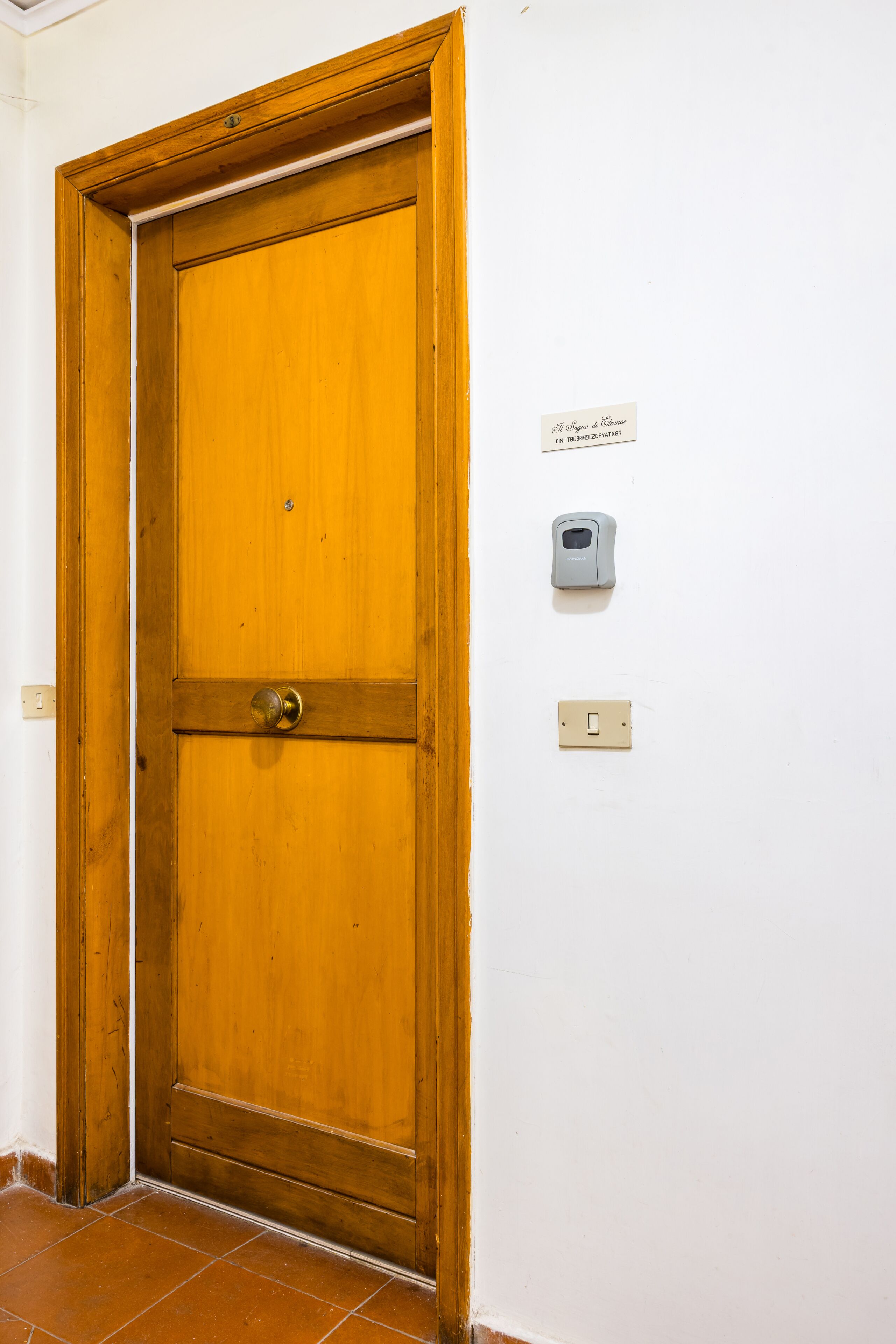 A wooden door with a brass doorknob, a wall-mounted intercom, and a light switch.
