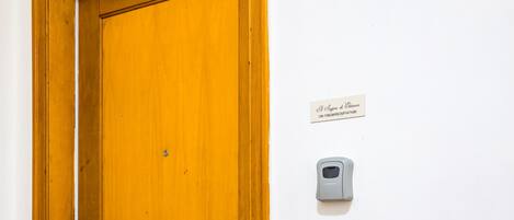 A wooden door with a brass doorknob, a wall-mounted intercom, and a light switch.