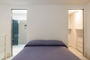 Een slaapkamer met een bed, een deur naar een badkamer en uitzicht op een douchegedeelte.