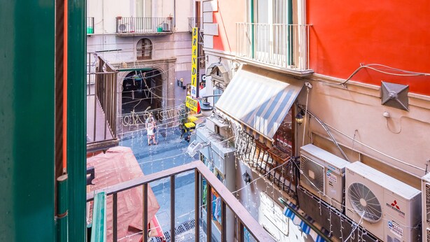 A narrow street with buildings on either side, a visible storefront with outdoor seating, and a pedestrian walkway. - Chiaia Prestige by NapoliApartments (Naples)