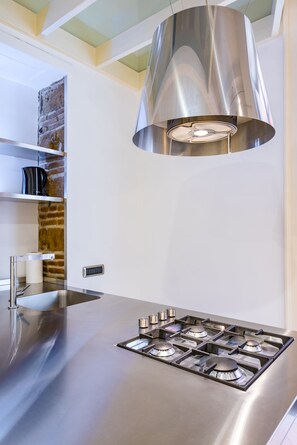 Een moderne keuken met een roestvrijstalen afzuigkap, een ingebouwde gasplaat en een accentmuur van baksteen.
