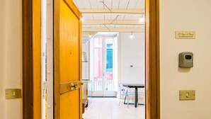 A hotel corridor with a wooden door, a sign indicating the room number, a table with chairs, and a window with blinds. - Chiaia Prestige by NapoliApartments (Naples)