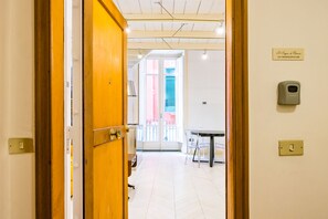 A hotel corridor with a wooden door, a sign indicating the room number, a table with chairs, and a window with blinds. - Chiaia Prestige by NapoliApartments (Naples)