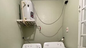 Ein Waschraum mit zwei Waschmaschinen mit Frontlader, einem übereinander gestapelten Waschtrockner und einem an der Wand montierten Warmwasserbereiter.