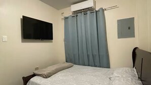 Ein Schlafzimmer mit einem Bett, einem Fernseher, einer Klimaanlage und einem Fenster mit Vorhängen.