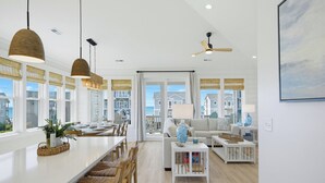 Un vaste espace de vie doté d’une grande fenêtre, d’un ventilateur de plafond et d’un coin repas avec une longue table.