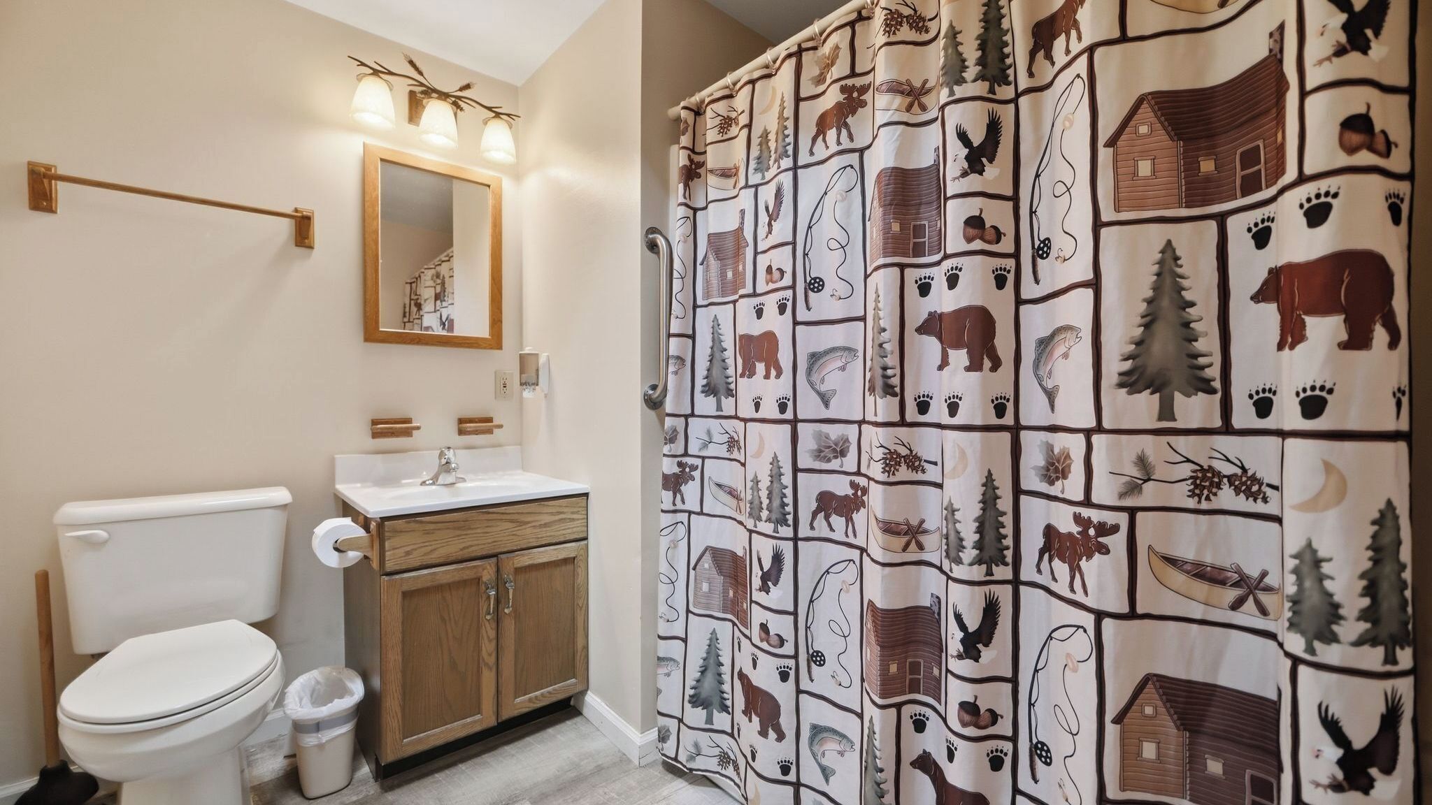 A bathroom with a toilet, sink, mirror, and shower curtain with wildlife patterns.