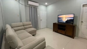Ein Wohnzimmer mit einem beigefarbenen Sofa, einem Fernseher auf einem Holzschrank und einer Tür.