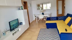 Een knus woongedeelte met een bank, een televisie, een eettafel en een spiegel.