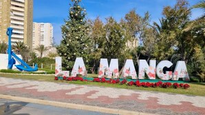 Een bord met de tekst 'LA MANGA' in grote letters, omgeven door begroeiing en een blauw sculptuur.
