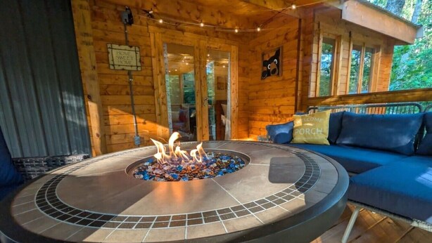 Una fogata circular con leña ardiendo, un sofá azul y paredes de madera.