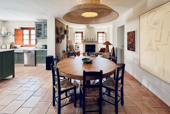 Een eetruimte met een ronde houten tafel, zwarte stoelen en een geweven plafondlamp.