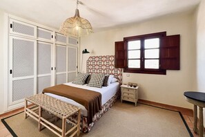 Ein Schlafzimmer mit Bett, Nachttisch, einer Pendelleuchte, einem Fenster mit Fensterläden und einem Schrank mit Lochmuster.