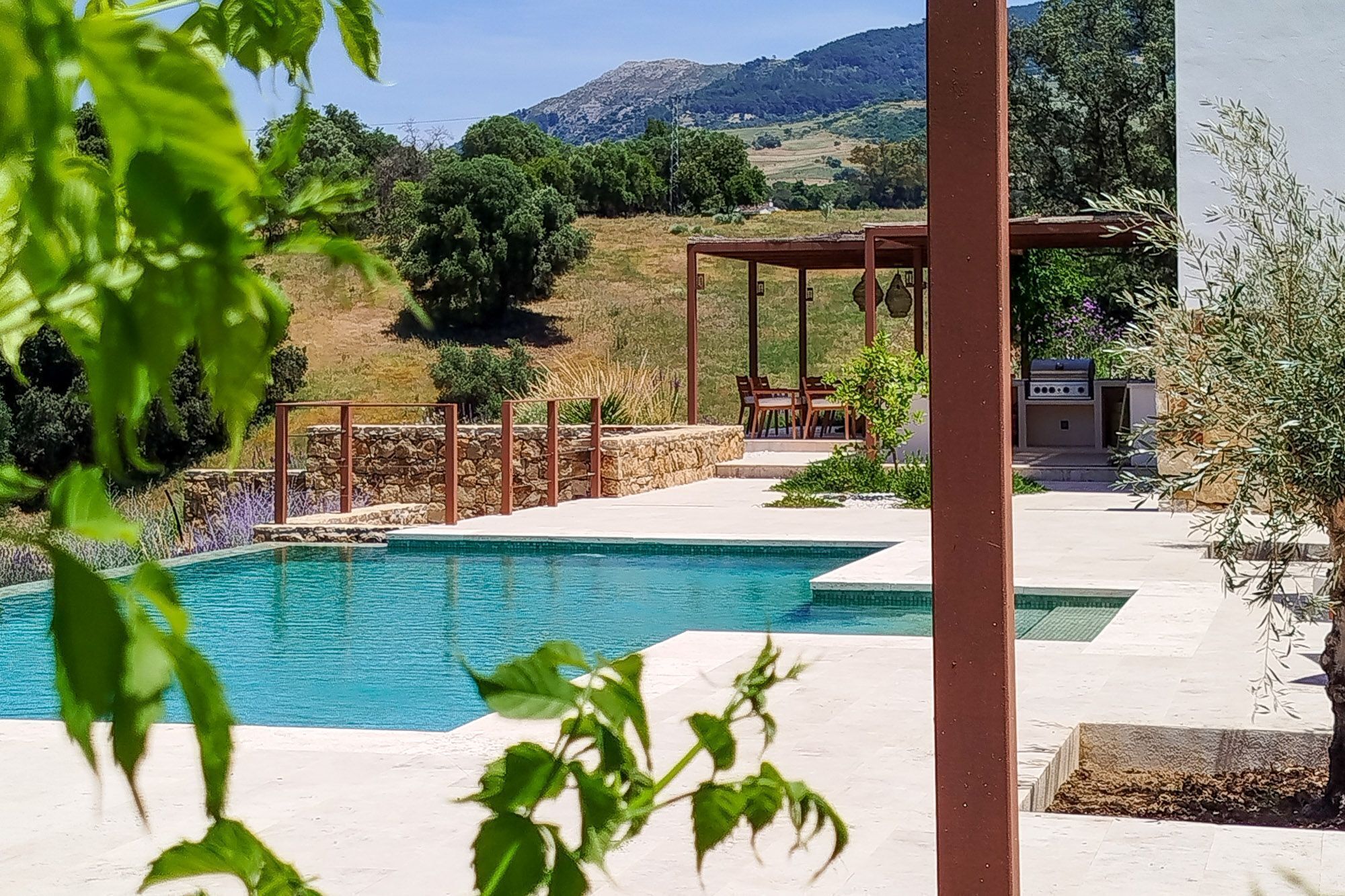 Une piscine agrémentée d’une pergola et d’un espace salon extérieur, le tout entouré de verdure et de collines.
