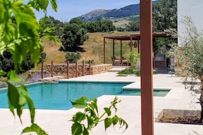 Ein Schwimmbecken mit einer Pergola und einer Sitzgelegenheit im Freien, umgeben von Grünflächen und Hügeln.