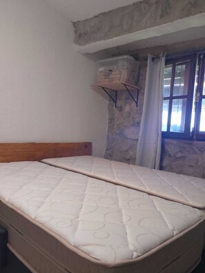 Una habitación con una cama, una ventana con cortinas y una pared de piedra.