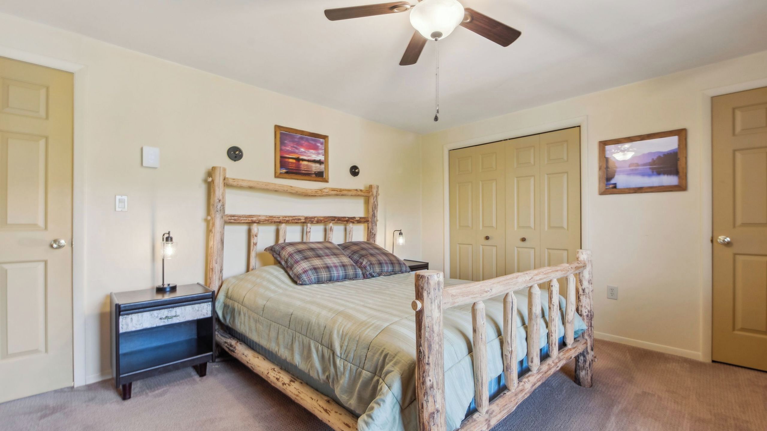 A bedroom with a wooden bed frame, a nightstand, a ceiling fan, and two doors.