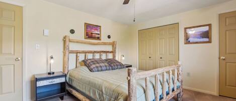 A bedroom with a wooden bed frame, a nightstand, a ceiling fan, and two doors.