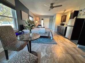Quarto moderno com cama, área de estar com poltrona e mesa, cozinha e sala de jantar.