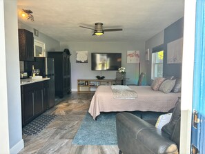 Ein Schlafzimmer mit einem Bett, einem Schreibtisch, einem Stuhl, einem Fernseher und einem Deckenventilator.