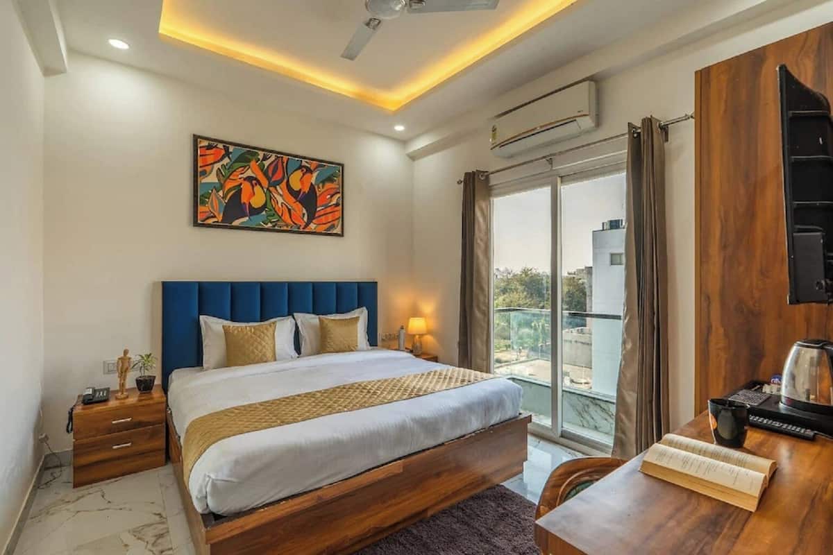 A hotel room with a bed, a desk, a chair, a painting, a window, and an air conditioning unit.