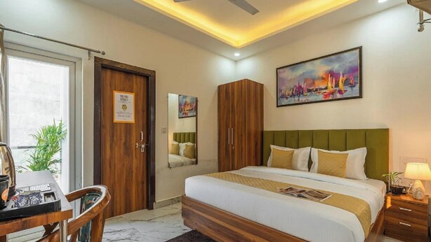 A hotel room with a bed, a desk, a chair, a mirror, a wardrobe, and a painting on the wall. - Coco House (Greater Noida)