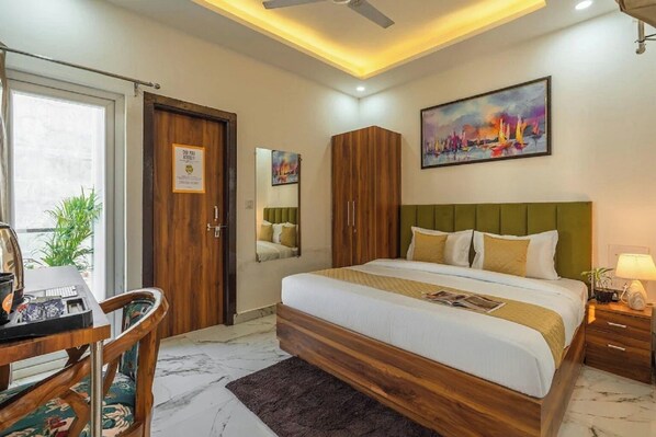 Una habitación de hotel con cama, escritorio, silla, espejo, armario y un cuadro en la pared.