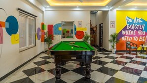 A billiards table in a lobby with a checkered floor, a ceiling fan, and a motivational quote on the wall. - Coco House (Greater Noida)