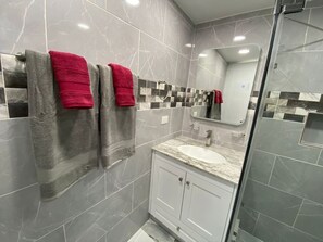 Een badkamer met grijze marmertegeltjes, een witte wasbak en twee handdoeken, één rood en één grijs.