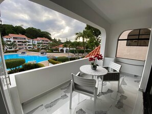 A balcony with a table and chairs, a view of a swimming pool, and a building with red roofs in the background. - Beautiful Sapphire Suite (Sosúa)