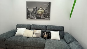 A modern living room with a gray sectional sofa, a cityscape painting, and a green arrow decoration on the wall. - Ler & Le Pety Palace Madrid gran vía  (Madrid)