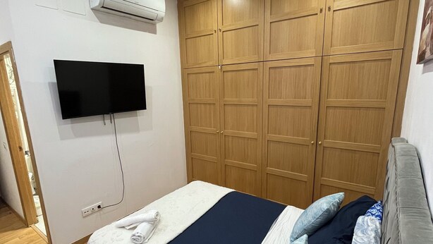 A bedroom with a bed, a TV, wooden wardrobe, and an air conditioning unit. - Ler & Le Pety Palace Madrid gran vía  (Madrid)