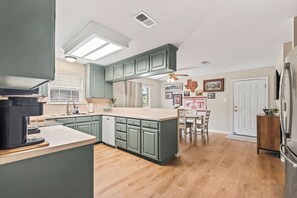 A kitchen with a central island, green cabinets, a refrigerator, and a dining area with a table and chairs.